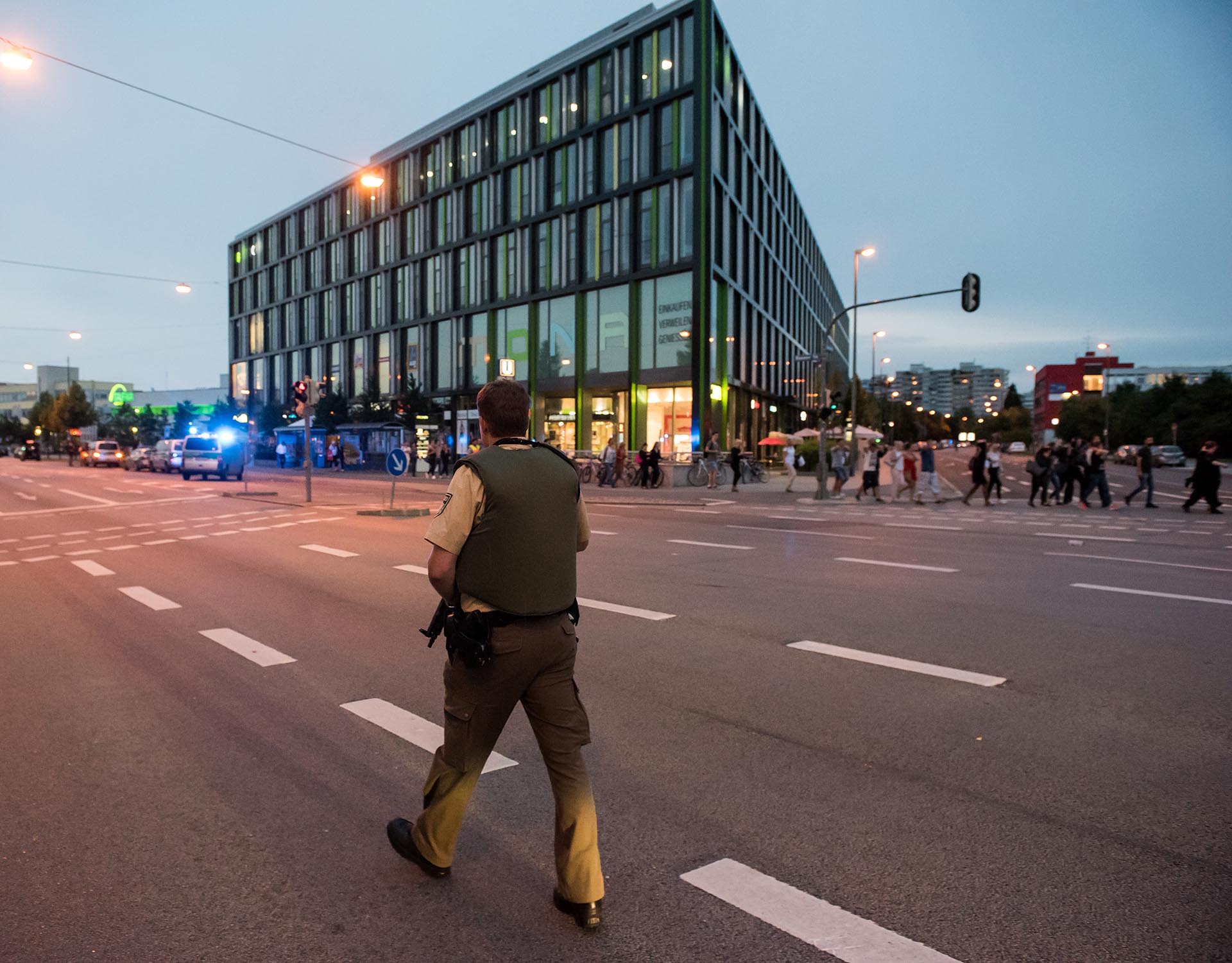 A policeman patrols as people are beeing evacuated (R) from a shopping mall in Munich on July 22, 2016 following a shooting earlier. At least one person has been killed and 10 wounded in a shooting at a shopping centre in Munich on Friday, German police said. / AFP PHOTO / STRINGER